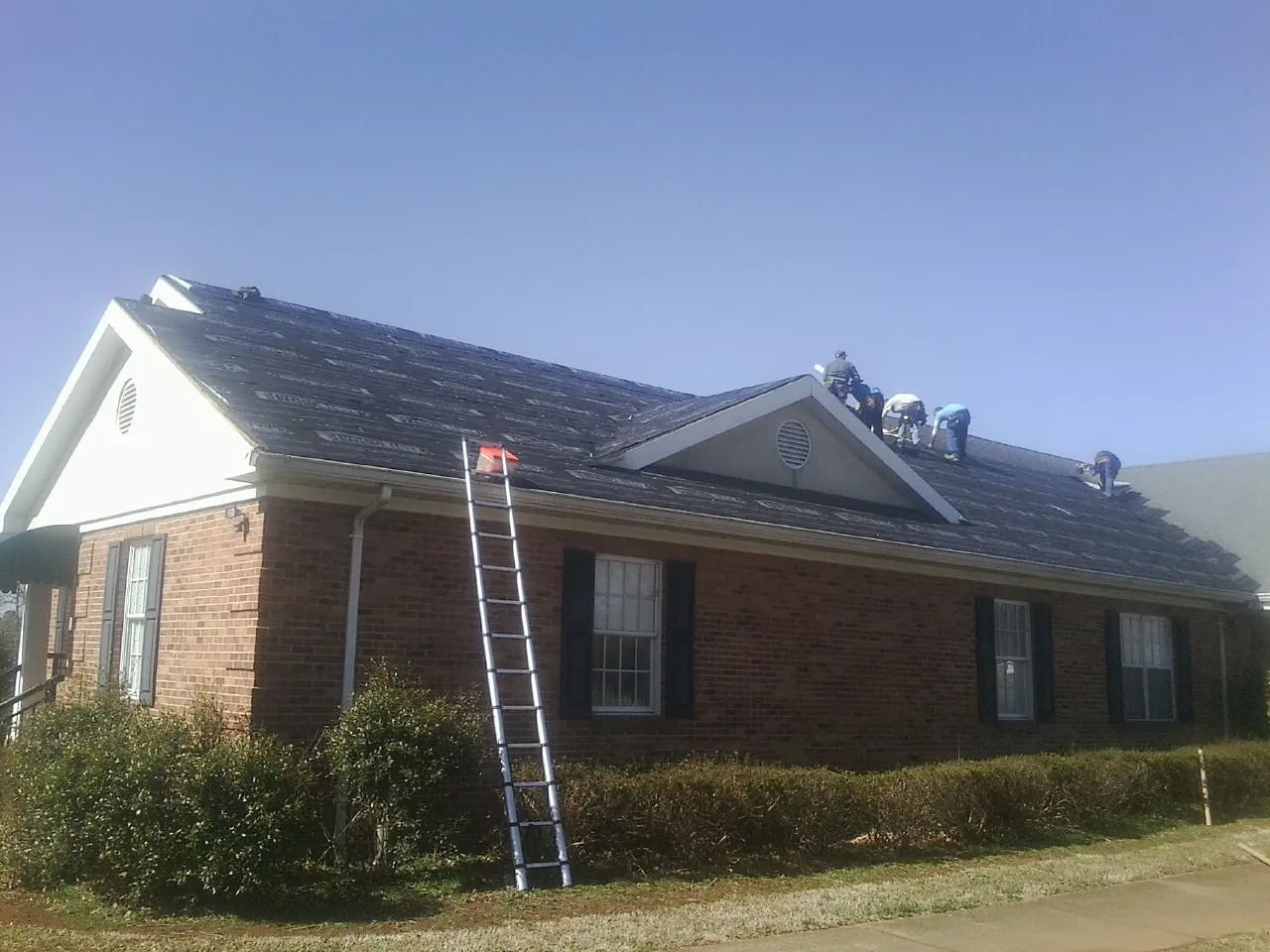 Crew tearing shingles off a brick ranch roof with a ladder set — Emergency Roof Repair work by our crew in Leavittsburg