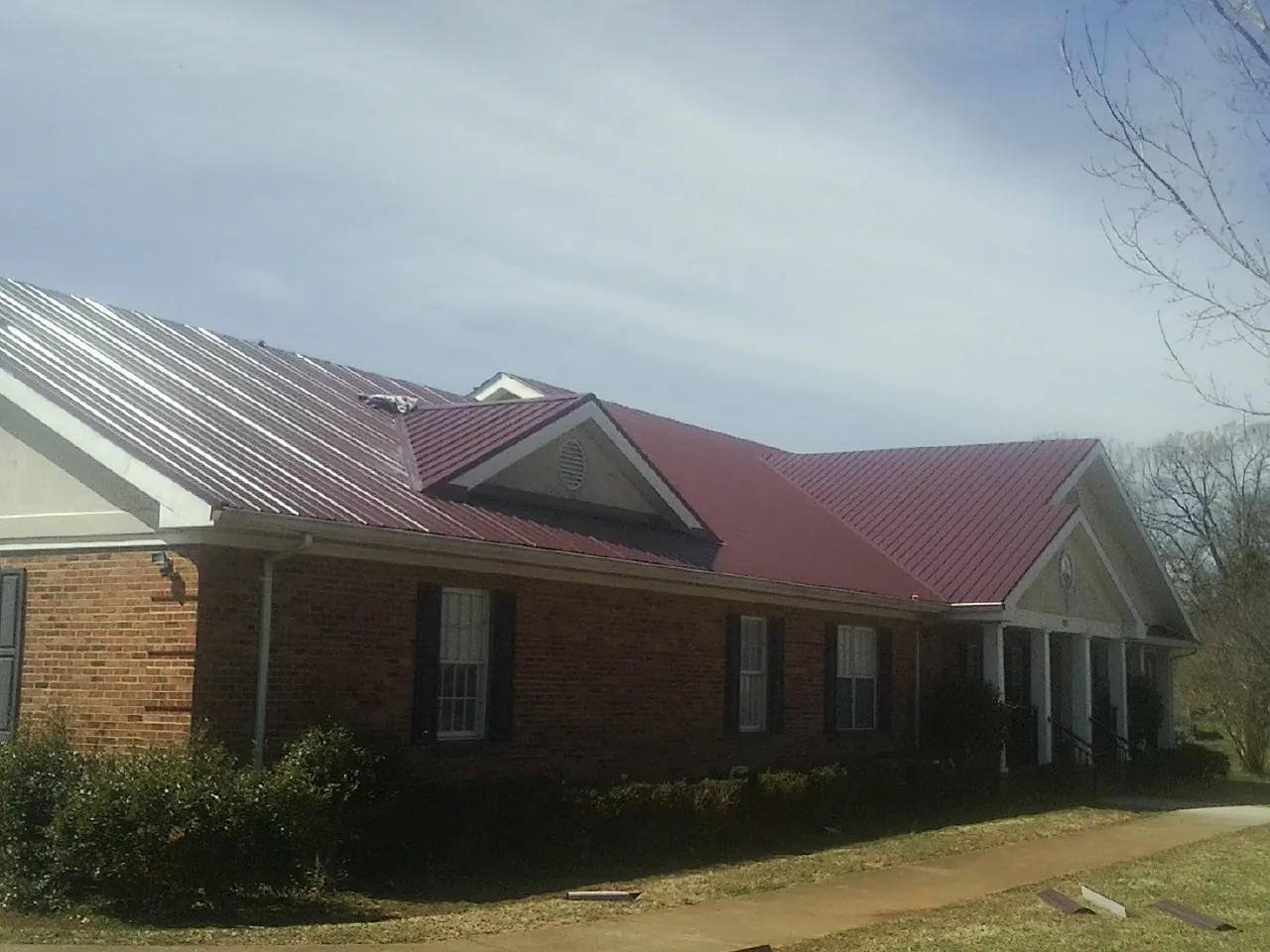 Red metal roof with gabled entries on a long brick building, from a Hail Damage Roof Repair job in Leavittsburg