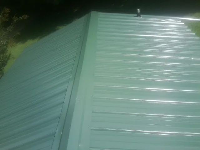 New green metal panels meeting at the ridge of a roof — Flat Roof Repair work by our crew in Leavittsburg