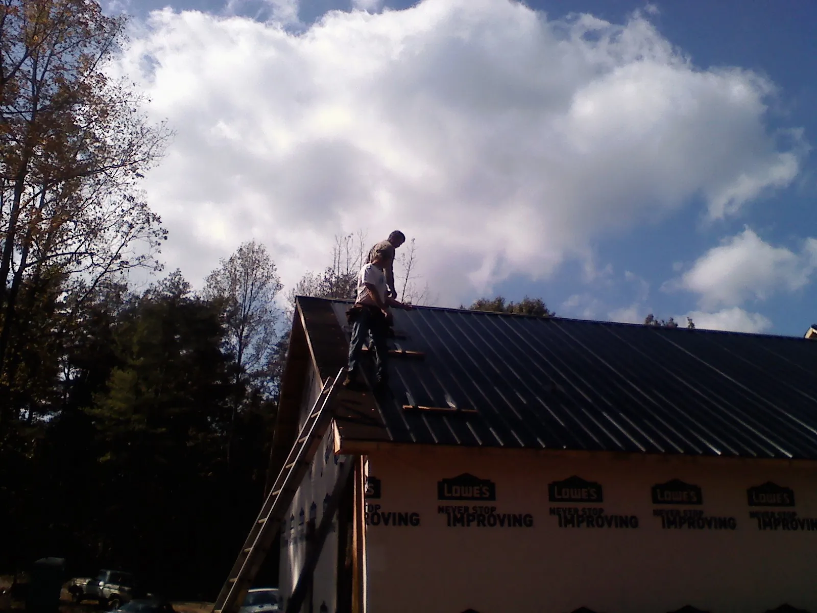 Roofer fastening dark metal panels high against a cloudy sky, from a Roof Inspection job in Leavittsburg