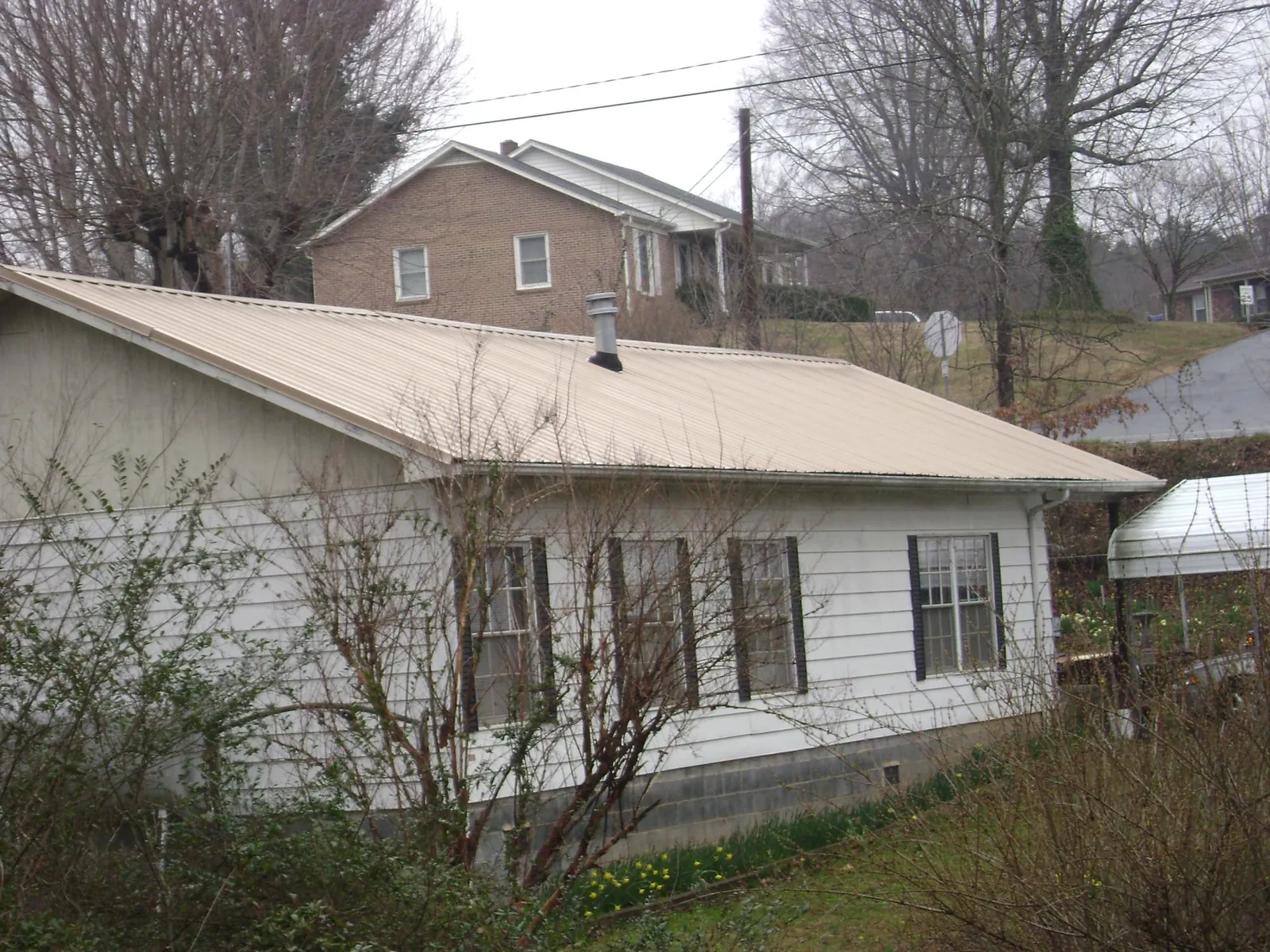Tan metal roof on a white sided house set into a hillside — Commercial Roofing by Roofing Brothers in Leavittsburg